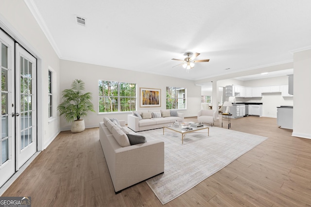 living room with crown molding, french doors, ceiling fan, and light wood-type flooring