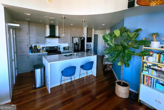 kitchen featuring decorative light fixtures, a center island with sink, black appliances, and wall chimney range hood