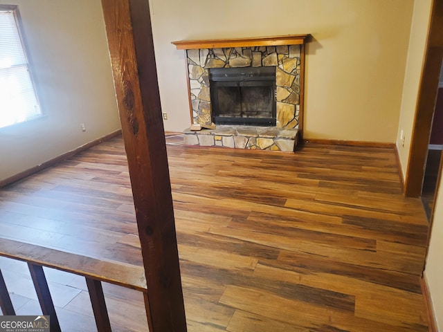 unfurnished living room featuring wood-type flooring and a stone fireplace