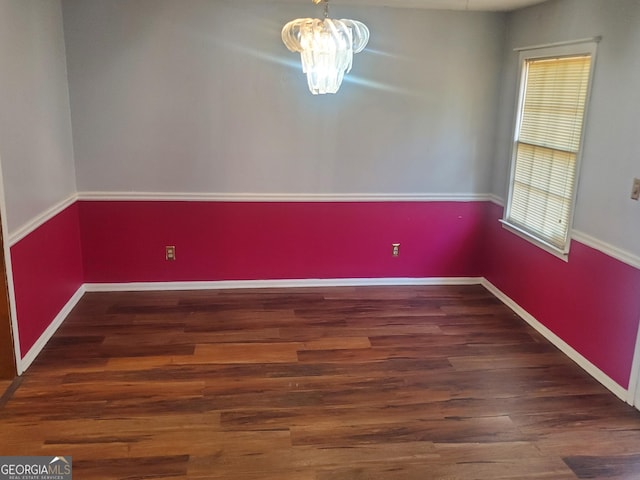 spare room with a notable chandelier and dark wood-type flooring