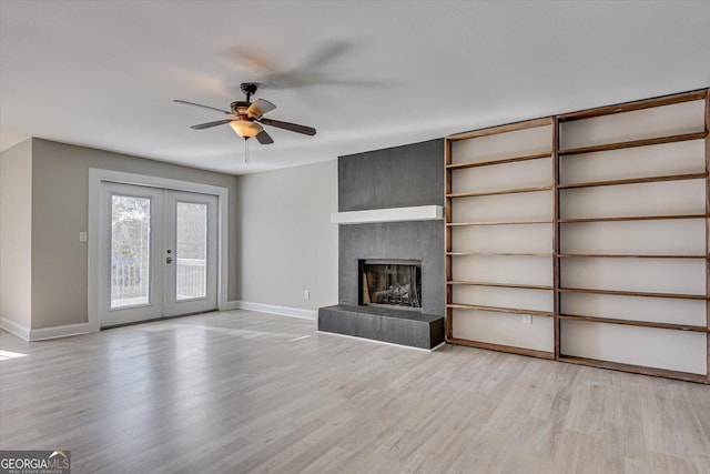 unfurnished living room with a large fireplace, ceiling fan, french doors, and light wood-type flooring