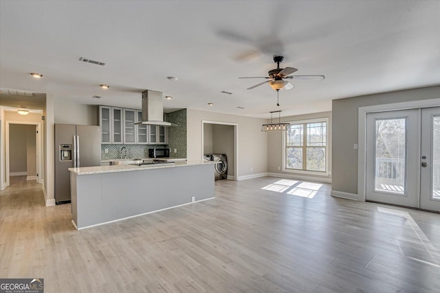 kitchen featuring wall chimney range hood, light wood-type flooring, tasteful backsplash, washer / dryer, and stainless steel fridge with ice dispenser