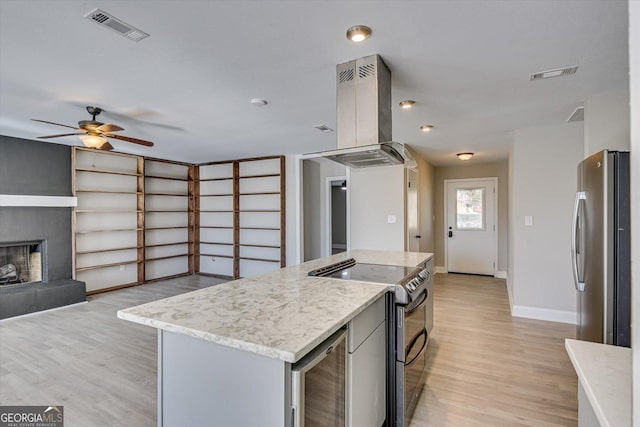 kitchen with appliances with stainless steel finishes, light wood-type flooring, a center island, wine cooler, and range hood