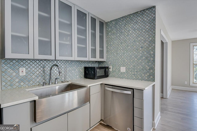 kitchen featuring decorative backsplash, sink, stainless steel dishwasher, and light hardwood / wood-style floors