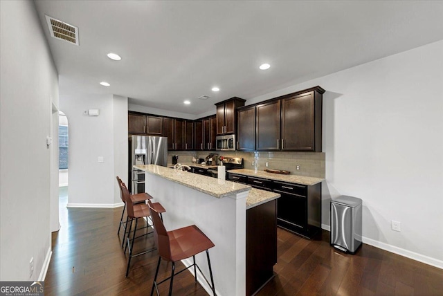 kitchen featuring light stone countertops, a kitchen island, stainless steel appliances, a kitchen breakfast bar, and dark brown cabinets