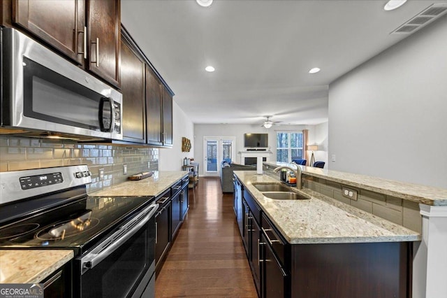 kitchen featuring dark wood-type flooring, sink, appliances with stainless steel finishes, and an island with sink