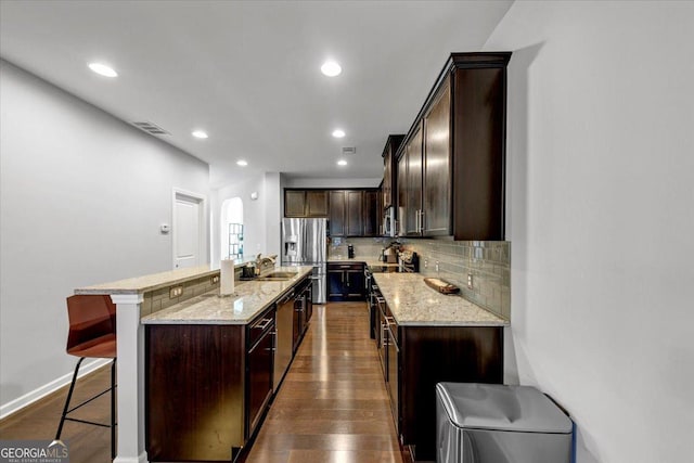 kitchen with a kitchen bar, a center island with sink, appliances with stainless steel finishes, dark wood-type flooring, and light stone counters