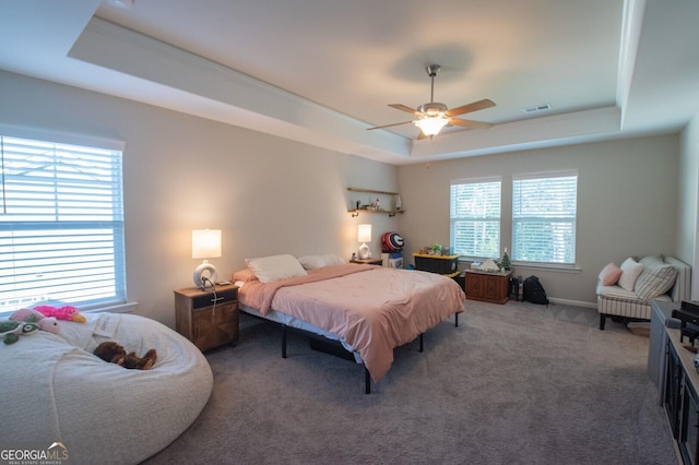 carpeted bedroom with a raised ceiling and ceiling fan