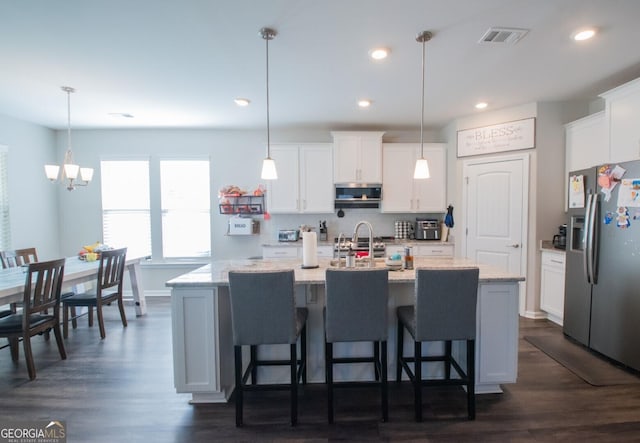 kitchen with dark hardwood / wood-style flooring, a center island with sink, pendant lighting, and appliances with stainless steel finishes