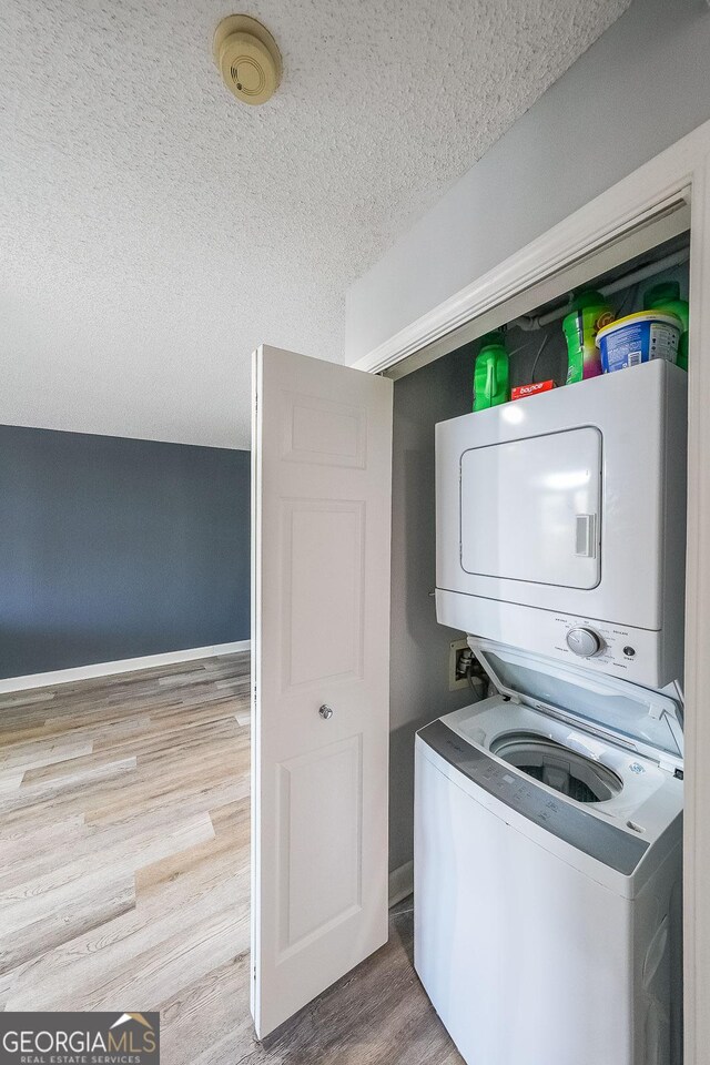 washroom featuring a textured ceiling, light hardwood / wood-style floors, and stacked washer and clothes dryer