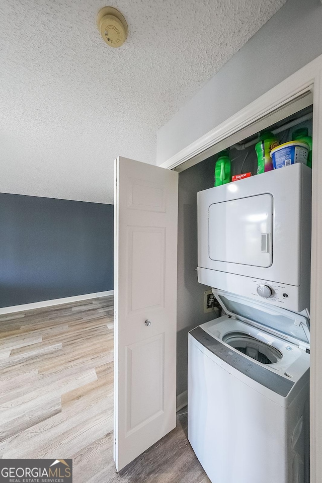 laundry area featuring stacked washer / drying machine, a textured ceiling, and light wood-type flooring