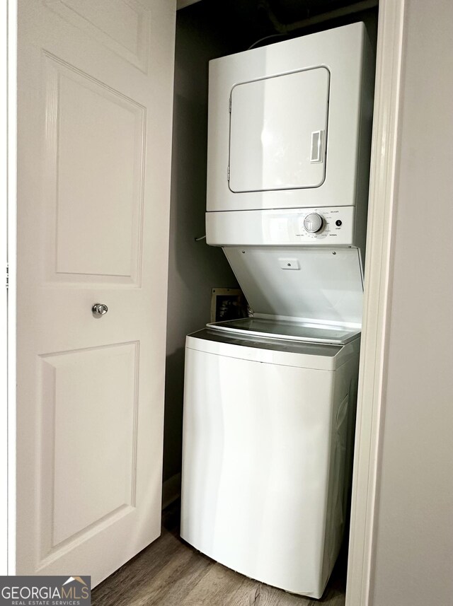 clothes washing area with stacked washer / drying machine, wood finished floors, and laundry area