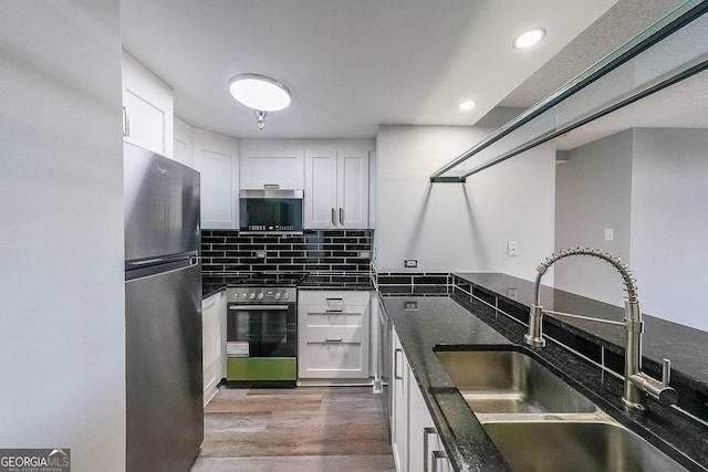 kitchen with sink, light wood-type flooring, appliances with stainless steel finishes, dark stone counters, and white cabinets