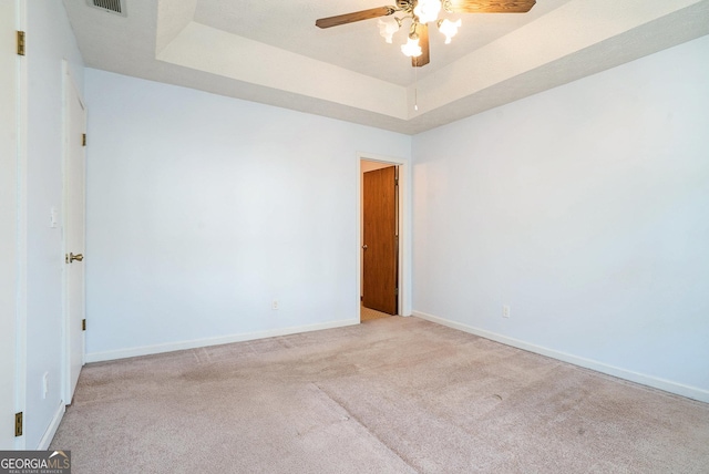 spare room featuring a tray ceiling, ceiling fan, and light colored carpet