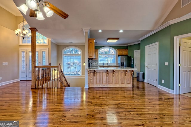 kitchen featuring stainless steel refrigerator with ice dispenser, decorative backsplash, dark hardwood / wood-style floors, crown molding, and ceiling fan with notable chandelier