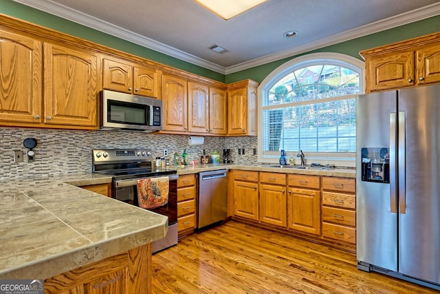 kitchen with appliances with stainless steel finishes, decorative backsplash, sink, ornamental molding, and light wood-type flooring