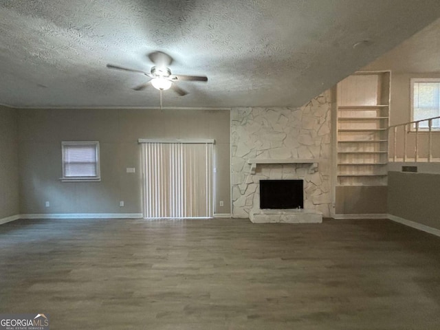 unfurnished living room with a stone fireplace, hardwood / wood-style floors, ceiling fan, a textured ceiling, and built in shelves