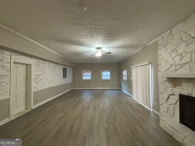 unfurnished living room with dark wood-type flooring, a textured ceiling, ornamental molding, ceiling fan, and a stone fireplace