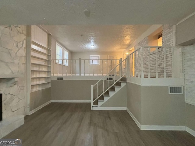 basement featuring built in shelves, a textured ceiling, and dark hardwood / wood-style floors