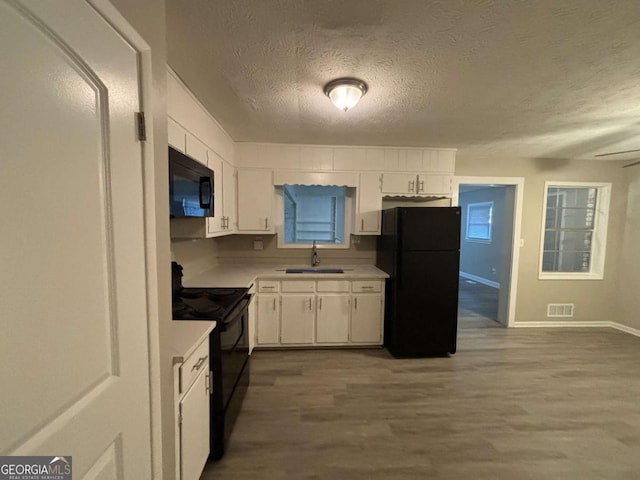 kitchen featuring a textured ceiling, black appliances, hardwood / wood-style floors, white cabinets, and sink