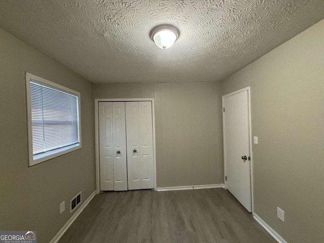 unfurnished bedroom with a textured ceiling, a closet, and wood-type flooring