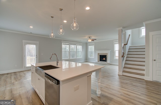 kitchen featuring stainless steel dishwasher, sink, white cabinetry, a center island with sink, and a stone fireplace