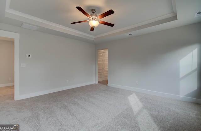 carpeted empty room with a raised ceiling, ceiling fan, and ornamental molding