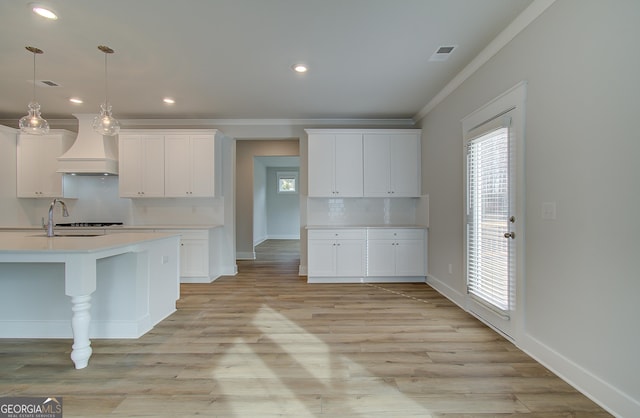 kitchen featuring pendant lighting, premium range hood, white cabinets, crown molding, and decorative backsplash