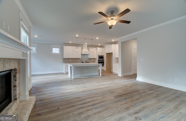 unfurnished living room featuring a fireplace, ceiling fan, ornamental molding, and sink