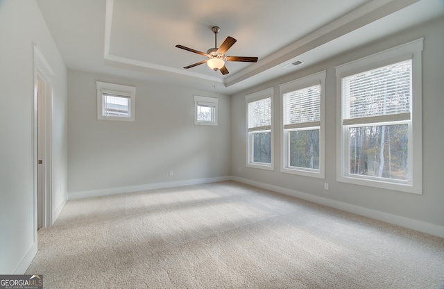 spare room with light carpet, a tray ceiling, and ceiling fan