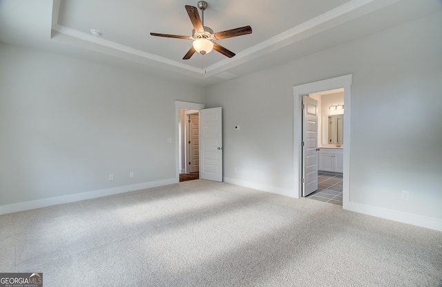 unfurnished bedroom featuring a tray ceiling, connected bathroom, ceiling fan, and light carpet