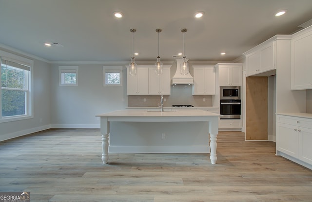 kitchen with appliances with stainless steel finishes, custom range hood, a kitchen island with sink, sink, and pendant lighting