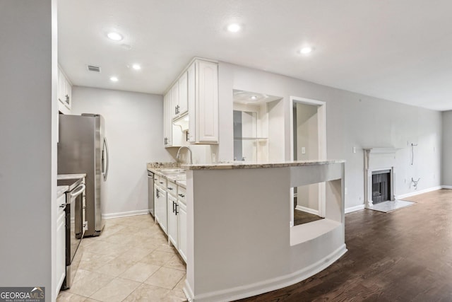 kitchen with light stone countertops, light wood-type flooring, stainless steel appliances, sink, and white cabinetry