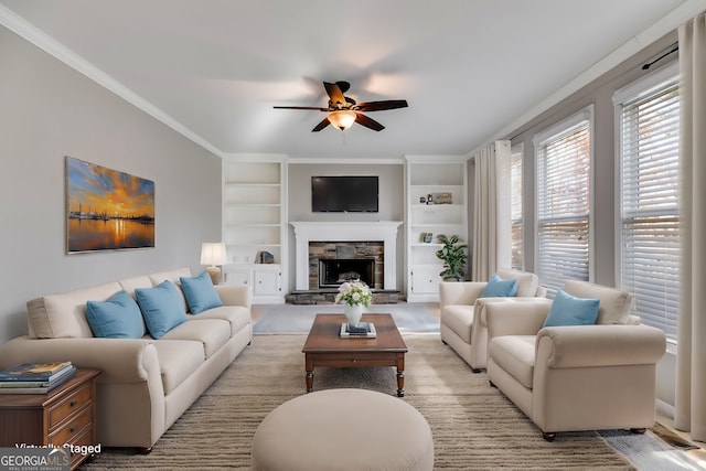 living room with ornamental molding, a stone fireplace, built in features, and ceiling fan