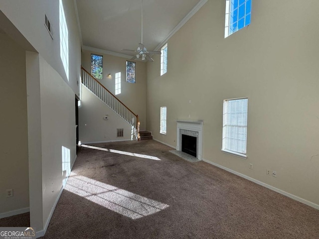 unfurnished living room with a healthy amount of sunlight, a towering ceiling, carpet floors, and ornamental molding