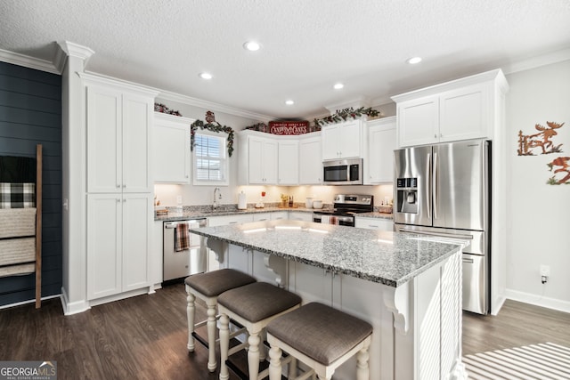 kitchen with light stone countertops, white cabinetry, stainless steel appliances, dark hardwood / wood-style flooring, and a kitchen island