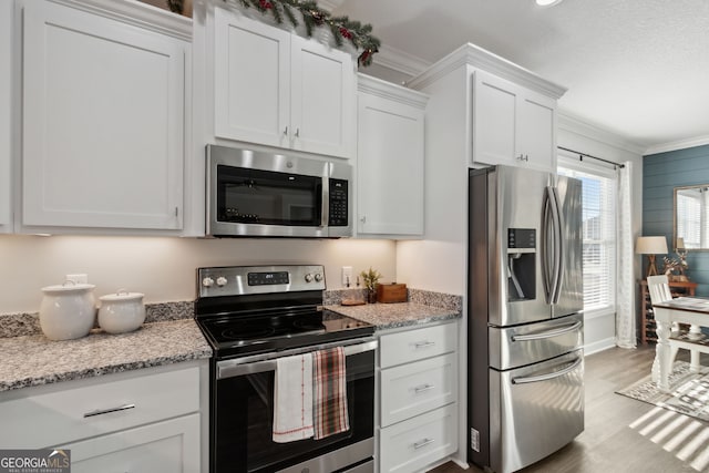 kitchen featuring light stone countertops, white cabinetry, stainless steel appliances, crown molding, and light wood-type flooring