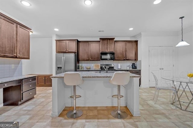 kitchen with a kitchen breakfast bar, stainless steel fridge, a center island with sink, and decorative light fixtures