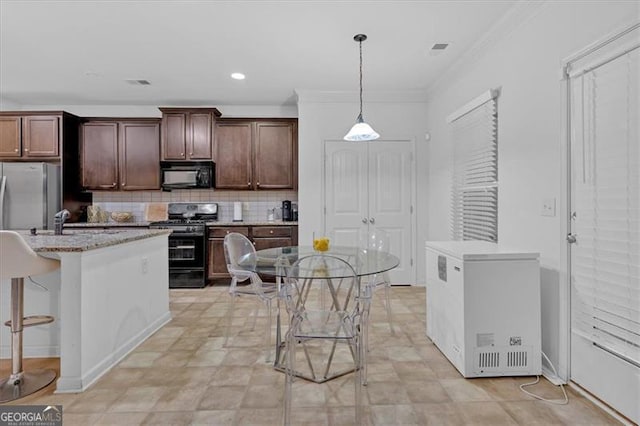 kitchen featuring a kitchen island with sink, black appliances, hanging light fixtures, decorative backsplash, and a breakfast bar area