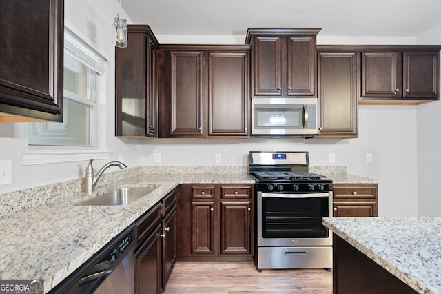 kitchen featuring dark brown cabinetry, sink, light stone counters, light hardwood / wood-style flooring, and appliances with stainless steel finishes