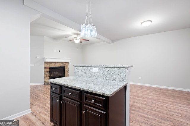 kitchen with pendant lighting, light hardwood / wood-style flooring, ceiling fan, a fireplace, and dark brown cabinets