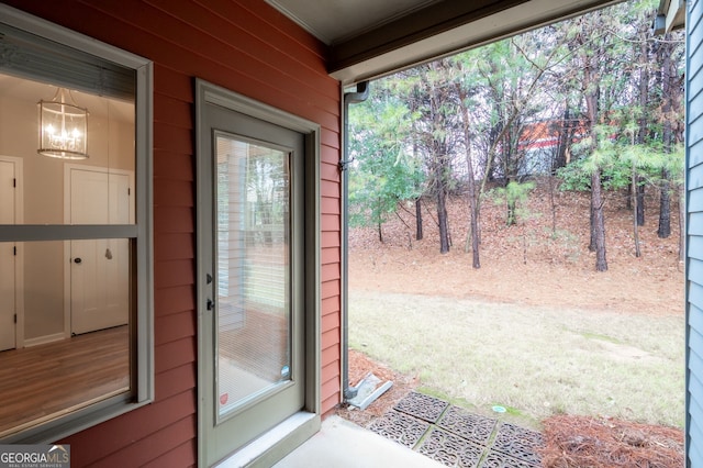 doorway featuring an inviting chandelier, wooden walls, and crown molding