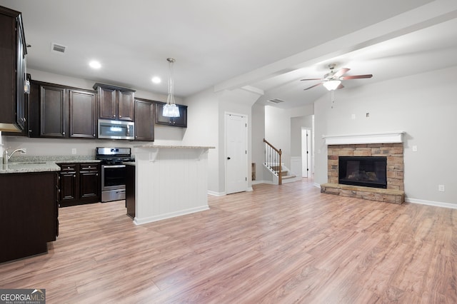 kitchen featuring ceiling fan, a stone fireplace, light hardwood / wood-style flooring, pendant lighting, and appliances with stainless steel finishes