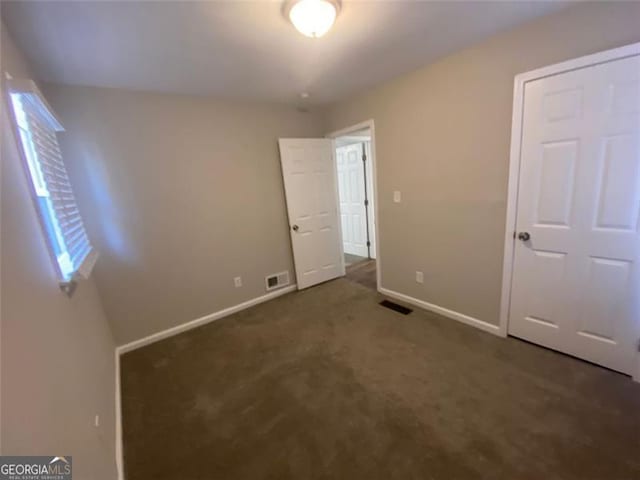 unfurnished bedroom featuring dark colored carpet and multiple windows