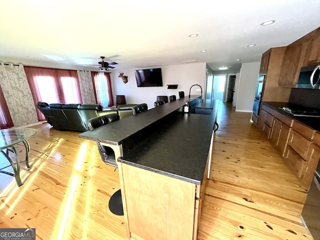 kitchen featuring black appliances, sink, light hardwood / wood-style flooring, ceiling fan, and a kitchen island