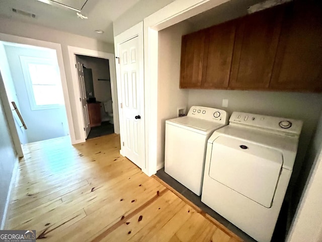 laundry area with light hardwood / wood-style floors, cabinets, and independent washer and dryer