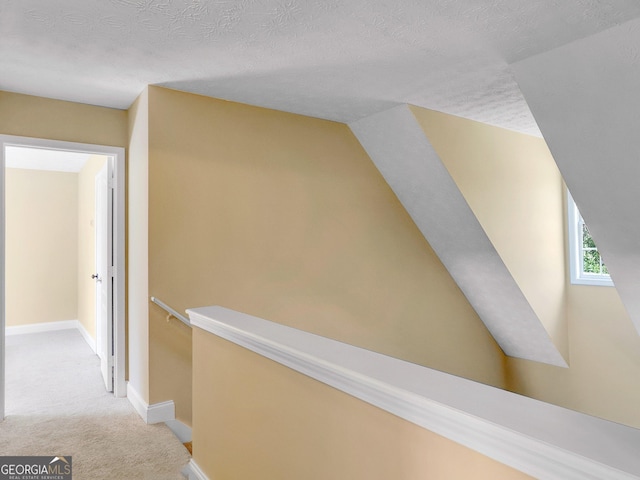 corridor featuring vaulted ceiling, light carpet, and a textured ceiling