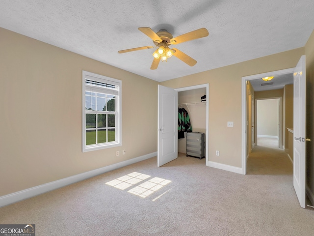 unfurnished bedroom with ceiling fan, a closet, light colored carpet, and a textured ceiling