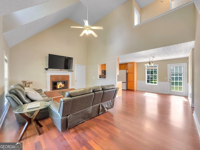 living room with a fireplace, wood-type flooring, ceiling fan with notable chandelier, and high vaulted ceiling