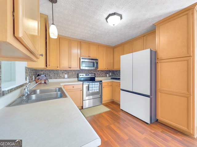 kitchen featuring sink, hanging light fixtures, a textured ceiling, appliances with stainless steel finishes, and light wood-type flooring